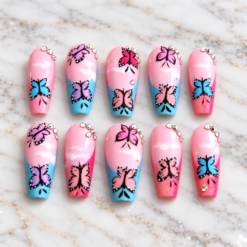 Set of 10 handmade butterfly press on nails in pastel pink and blue with glossy finish and crystal rhinestones, arranged on white marble.