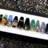 Black and gold coffin press-on nails in a tray, with a peacock feather nail, teal scales and zebra swirls