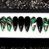 Black stiletto press on nails with four green and gold marble accent nails, displayed in a gift box