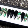 Glossy black stiletto press-on nails in a display tray, with green and gold marble accent nails