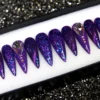 Dark purple glitter stiletto press-on nails in a tray, with a teardrop crystal on one nail and a metallic sheen