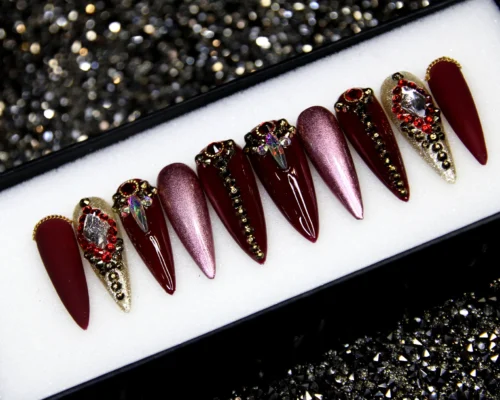 Oxblood stiletto press-on nails from the other end of the tray, with mauve chrome and jewelled champagne accent nails