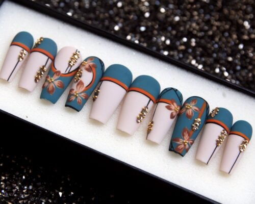 Matte cream and teal coffin press-on nails in a tray, with burnt orange stripes, painted flowers and gold beads