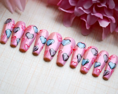 Side angle of pink coffin press-on nails on woven cloth, showing blue, grey and red outlined hearts and a glossy finish