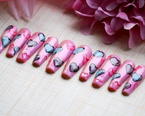 Ten long coffin press-on nails on linen beside a pink flower, with painted blue and grey hearts and red heart outlines