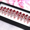 Ruby crystal press-on nails lined up in a black box, seen from the opposite side with pink flowers behind
