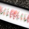 Floral stiletto press-on nails in a black tray, pink and clear with white blossoms, leaves and gold flecks