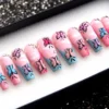 Angled view of pink and blue coffin press-on nails with painted butterflies and small rhinestones in a glitter-lined tray