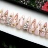 Sheer nude stiletto press-on nails in a tray, with rhinestone clusters, gold stars and a crescent moon