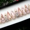 Nude glitter press-on nails from the other end of the tray, with crystal clusters and tiny gold stars, red flowers behind