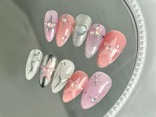 Pink, lilac and silver chrome press-on nails resting on a glass tray, with raised stars and rhinestone details