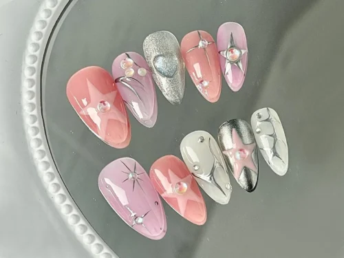 Pink and lilac press-on nails on a round glass tray in a mirrored layout, with chrome stars and pale gems