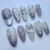 Almond press-on nails from another angle, showing a white painted butterfly wing, a silver heart charm and chain drapes