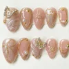 Pink cat-eye almond press on nails with gold-outlined bows, a rhinestone butterfly, pearls and 3D petals