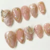 Blush pink almond press-on nails seen from the other side, with gold outlines, 3D bows and crystal butterflies
