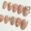Pink cat-eye press-on nails laid in two rows, with gold line art, pearls and rhinestone butterfly charms