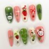 Coral, cream and green press-on nails from another angle, with a strawberry, a red bow, sparkle stars and a cat face