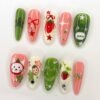 Green and coral almond press-on nails laid flat with a round grey forest creature, a white cat face and red strawberries
