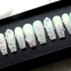 Aurora chrome press-on nails from the other end of the tray, white-to-mint shimmer with swirl ridges and pink gems