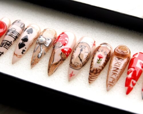 Nude stiletto press-on nails in a tray, hand-painted with a clock face, a playing-card spade, music notes and a rose
