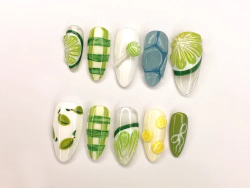 Lime and white almond press-on nails laid flat with painted lime slices, lemon wheels, green plaid and a lollipop