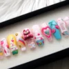 Angled view of pink glitter coffin press-on nails with a cherry heart, ice-cream swirls, a yellow cupcake nail, blue clouds