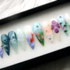 Angled view of koi press-on nails with a red-orange fish, green stems and tulips, a purple blossom and water-drop beads