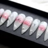 Milky white stiletto press-on nails in a black tray, with blush pink hearts, silver bows and tiny crystals
