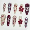 Cherry red and cream almond press-on nails laid flat with sculpted red flowers, silver pearl hearts and painted bows