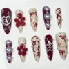 Ten red and cream press-on nails arranged differently on a plain backdrop, with glossy flowers, pearls and a looped heart