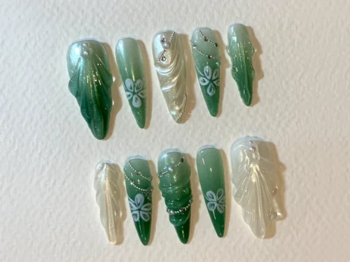 Green gradient stiletto press-on nails laid out from the other side, with flowers, bead chains and sheer white ridged nails