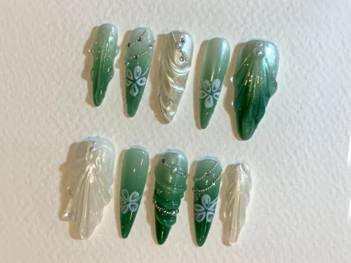 Jade green to white stiletto press-on nails on textured white paper, with pale flowers, pearls and rippled drapery