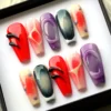 Coffin press-on nails in a black-edged box: glossy red with black 3D drips, purple oval frames, smoky teal and peach ombré