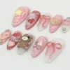 Pink almond press-on nails in a mirrored layout, with puffy heart nails, gem accents, a yellow star and a sheer ribbon