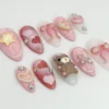 Pink glitter almond press-on nails flat on white, with a brown teddy bear, red hearts, a pale puffy star and a sheer bow