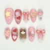 Pink glitter almond press on nails with a 3D teddy bear, a yellow KISS heart, a puffy star, sheer bows and gems