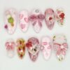 Pink almond press-on nails laid flat with a sculpted glitter bow, a gingham bow, hearts, lipstick kisses and a cat in a heart