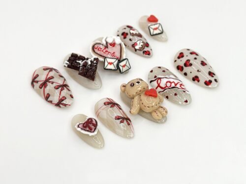 Valentine press-on nails laid flat from another side: leopard spots, red bows, love lettering and envelope charms