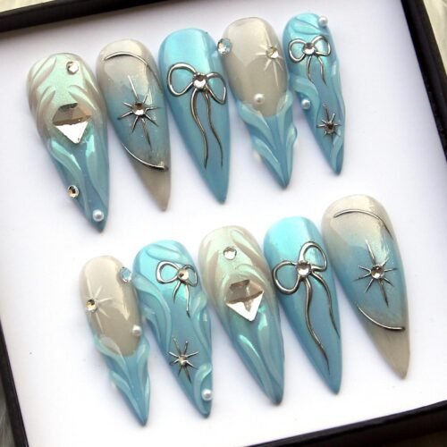 Angled view of icy blue stiletto press-on nails showing silver bow outlines, pearl dots and a diamond-cut gem