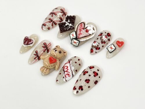 Cream and red almond press-on nails laid flat with a 3D teddy bear holding a heart, a chocolate bar and love letters