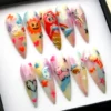 Pastel rainbow press-on nails in a black box from another side, with a bee, a sketched heart, a moon and stars
