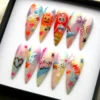Pastel rainbow stiletto press-on nails in a black box with a smiling sun, red-haired mermaid, pink pig and stars