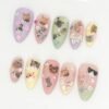 Pastel almond press-on nails in lilac, pink, sage and yellow on white, each with tiny cat photos, hearts and star sprinkles
