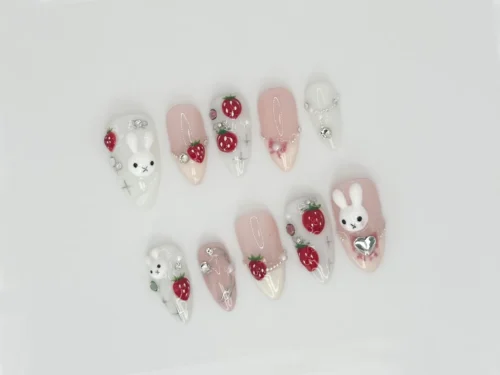 White and pink almond press-on nails laid flat with a sculpted white bunny, red 3D strawberries and silver gems