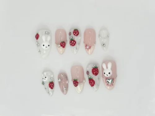 Pink and white press-on nails from another angle, with raised bunny faces, strawberries, a silver heart and small gems