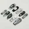 Black and white coffin press-on nails drawn with cartoon faces, a bunny, spirals and stripes, laid on a pale surface
