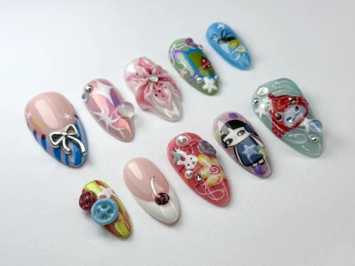 Pastel almond press-on nails on white: a silver bow on blue stripes, a pink 3D lily, buttons and small cartoon faces