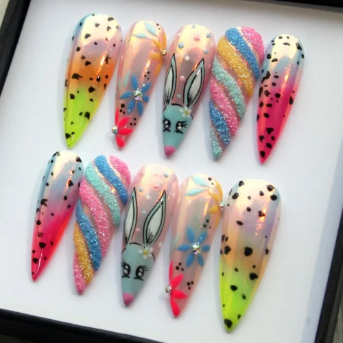 Stiletto press-on nails in a black display box: neon lime and pink ombré, black speckles and a painted blue bunny face