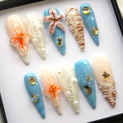 Beach press-on nails from another angle: blue gold-leaf nails, white pearl swirls, an orange flower and a starfish