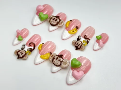 Monkey press-on nails from another angle, with pink stripes, white tips, banana charms and green heart nails